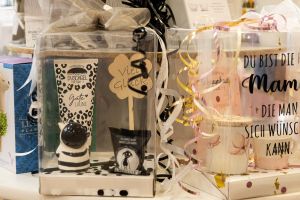Durchsichtige Geschenkverpackungen mit Duschgel, Kerzen und Tassen für Anlässe wie „Viel Glück“ und „Mama“.
