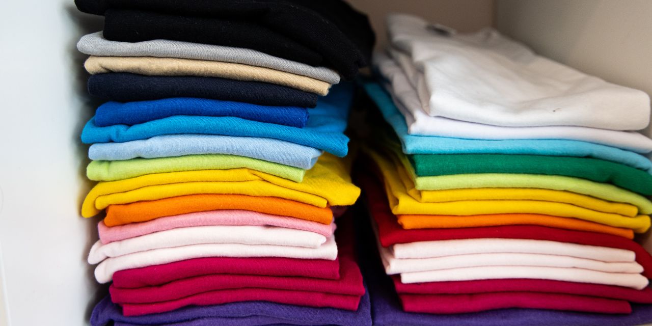 Zwei ordentliche Stapel farbiger T-Shirts nebeneinander in einem Schrankfach.