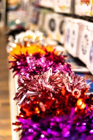 Eine Reihe glänzender, bunten Pompons aus metallischer Folie in Pink, Rot und Violett auf einer Regalkante.