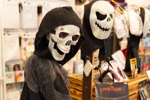 Eine Skelettfigur mit schwarzer Kapuze neben einer Totenkopfmaske und anderen Halloween-Artikeln