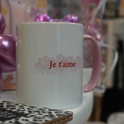 Weiße Tasse mit rosa Henkel und rotem „Je t'aime“-Schriftzug.