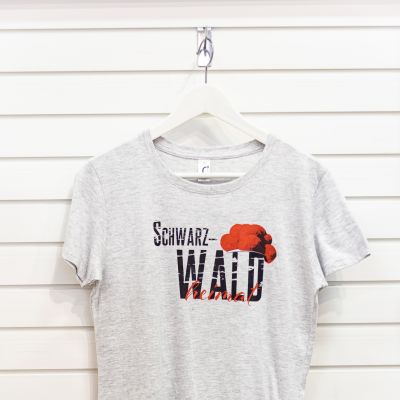 Weißes-Graues T-Shirt mit Motiv bestehend aus serifenlosen texturiertem schwarzem Aufdruck „Schwarz-WALD“, traditionellem roten Bollenhut und in roter Schreibschrift gesetztem „heimat“.
