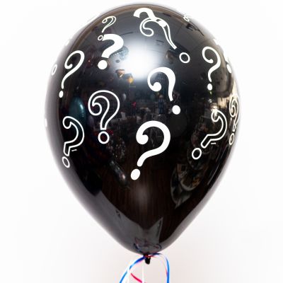 Schwarzer aufgeblasener Ballon mit Fragezeiten-Motiven. Verschlossen mit Geschenkbändern in verschiedenen Farben.
