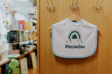 Wießes Babylätzchen in hellblauer Umrandung mit grafischem Aufdruck: „Maximilan“