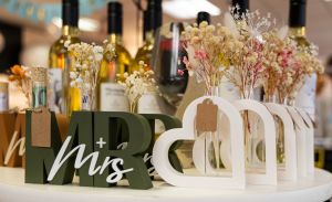 Dekorative Holzaufsteller mit dem Schriftzug „Mr + Mrs“ und Herzformen, bestückt mit kleinen Trockenblumensträußen.