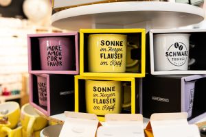 Bedruckte Keramiktassen in passenden Geschenkverpackungen, unter anderem mit dem Spruch „Sonne im Herzen, Flausen im Kopf“.