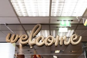 Champagnerfarbener Folienballon in Schreibschrift mit dem Wort „welcome“ unter der Ladendecke.